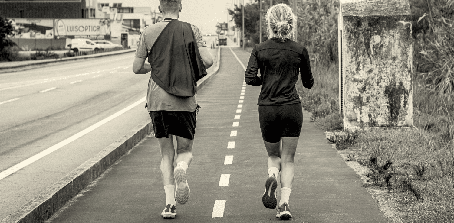 Two people jog side by side on a marked urban path, captured in black and white to highlight motion, routine, and connection.